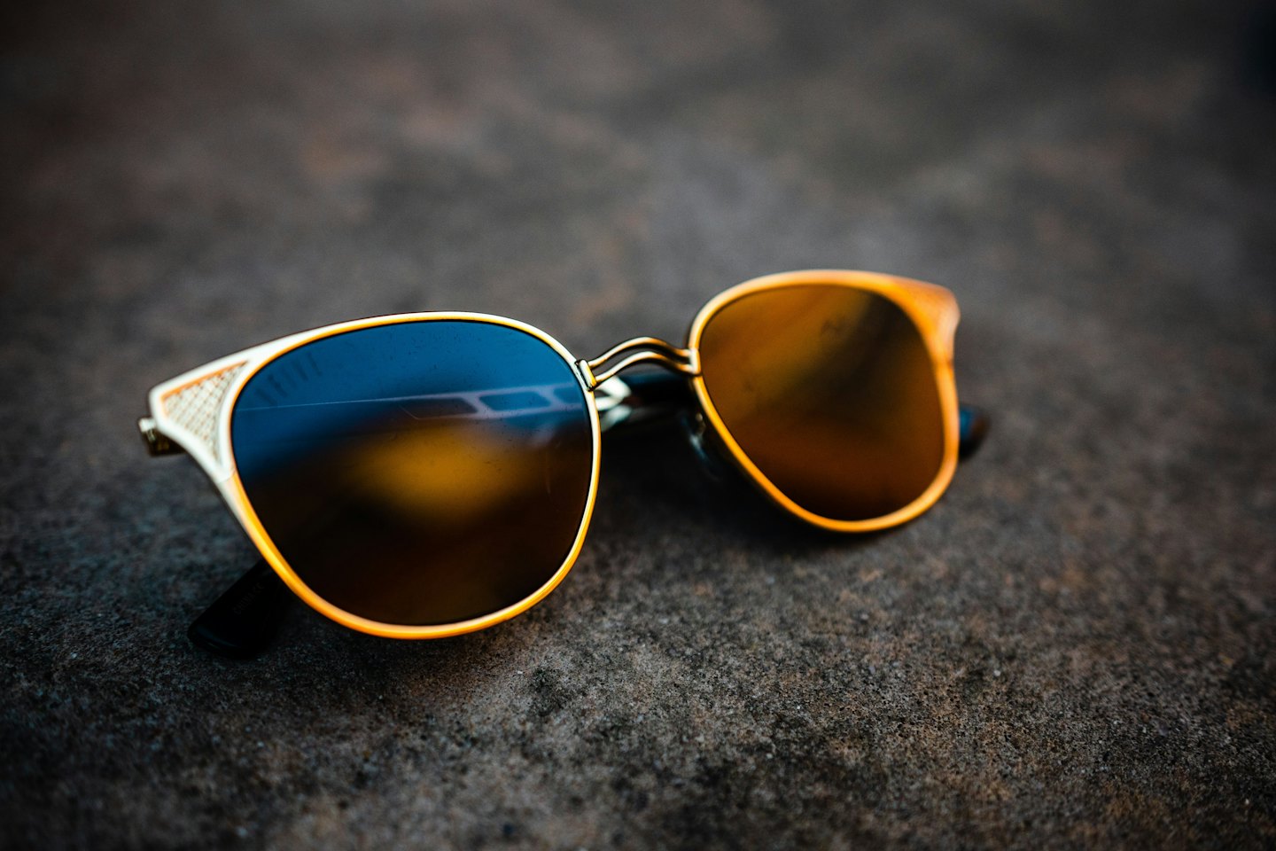 Gold framed sunglasses rest on a dark textured surface.